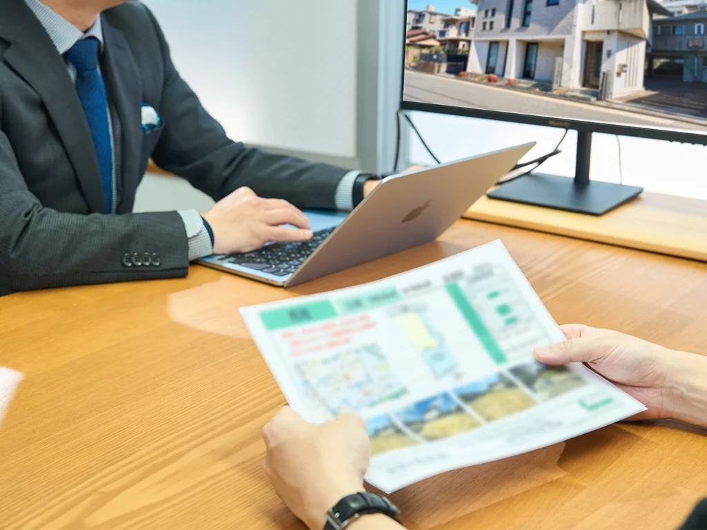 男性スタッフがパソコンを操作し、お客様が物件の資料を手に持っている。