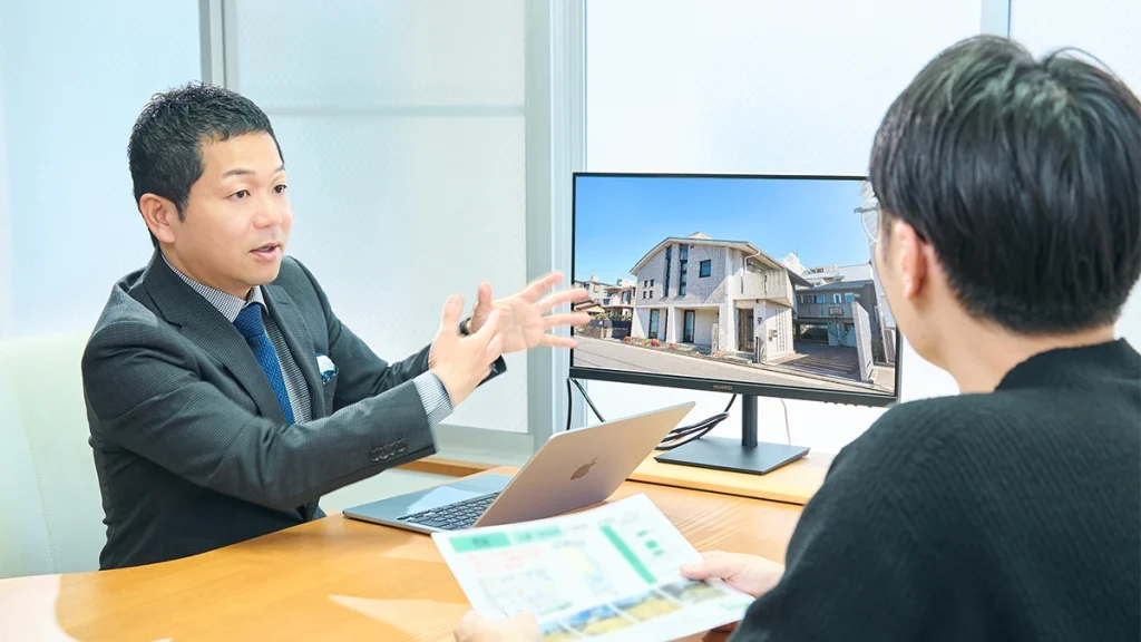 男性スタッフが物件を映したモニターを指し示しながら、お客様に対して説明をしている