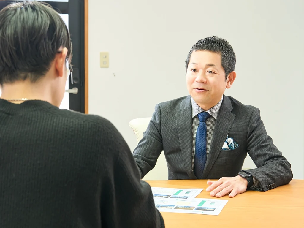 男性スタッフが机に物件情報を広げ、お客様に話をしている。